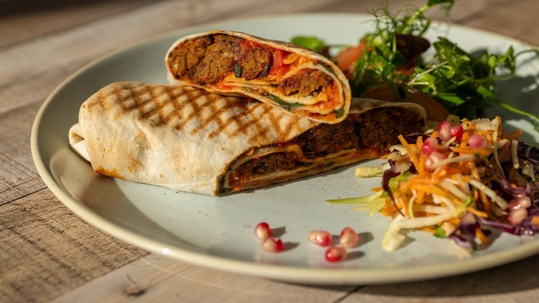 A plate with a toasted falafel and wrap and side salad and winter slaw