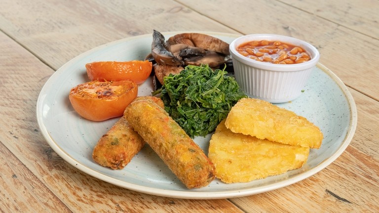 A plate with hashbrowns, beans, spinach, mushrooms, tomatoes and vegetarian sausages.