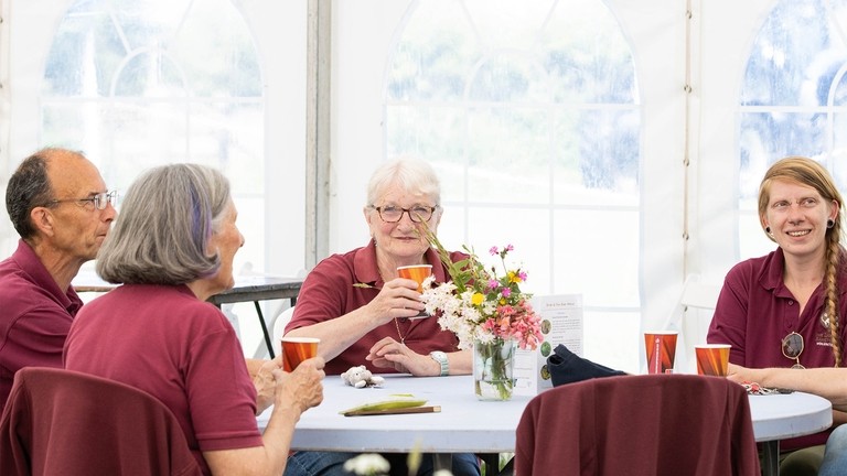 An image of a group of people wearing burgundy polo shirts sat at a circular table.