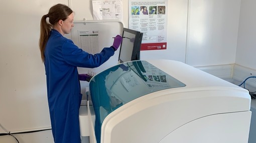 A women in blue scrubs working on a machine in a Pathology lab