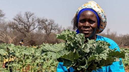 A women holding her crops whilst stood in front of her crop field
