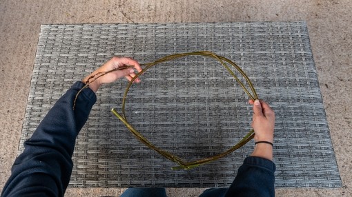A pair of hands shaping wooden twigs into a circle above a placemat