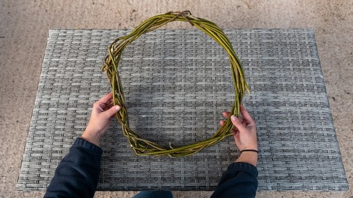 A pair of hands holding a finished base of a wreath featuring multiple twisted twigs