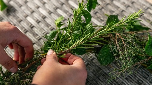 A pair of hands threading green leaves into the wooden twigs of a wreath