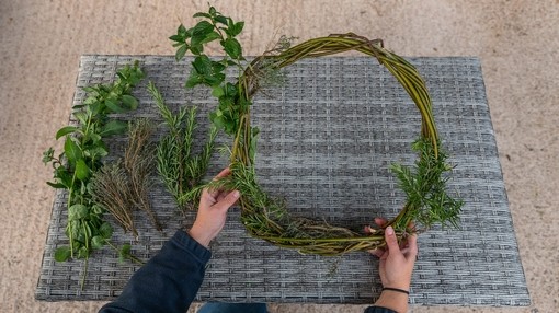 A pair of hands holding a partially finished wreath that is have filled with green leaves
