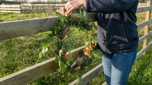 A pair of hands tying a winter wreath onto a wooden fence