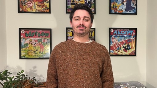 A dark haired man stood in front of a white wall with six square vinyl artwork covers hung up in two rows of three.