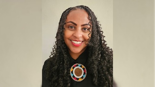 A selfie of women with curly black hair wearing a black shirt with a circular design on the collar.