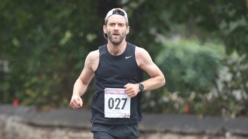 A man wearing a reversed cap and a black running vest with the number 027 pinned to the front.