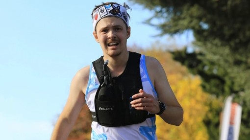 A man wearing a blue running top and head sweat band with a black running vest on top.