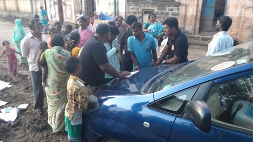 A group of people stood in front of a blue car.