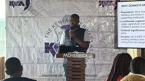 A man stood at a podium speaking into a microphone as he presents a PowerPoint in front of a crowd.