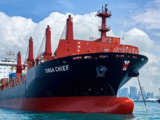 An image large red and black shipping boat sailing with a big city in the background.