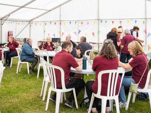 An image of groups of people wearing burgundy tops sat at circular tables under a white marquee.